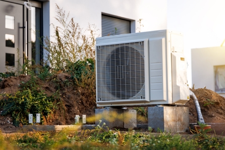 Outdoor unit of an air sourced heat pump in front of a newly built single-family home